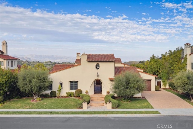 mediterranean / spanish-style home featuring driveway, a garage, stucco siding, a tile roof, and a front yard