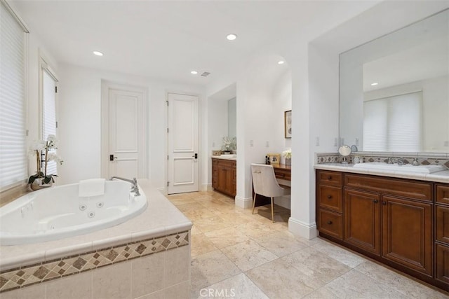 full bathroom with a tub with jets, two vanities, a sink, and recessed lighting