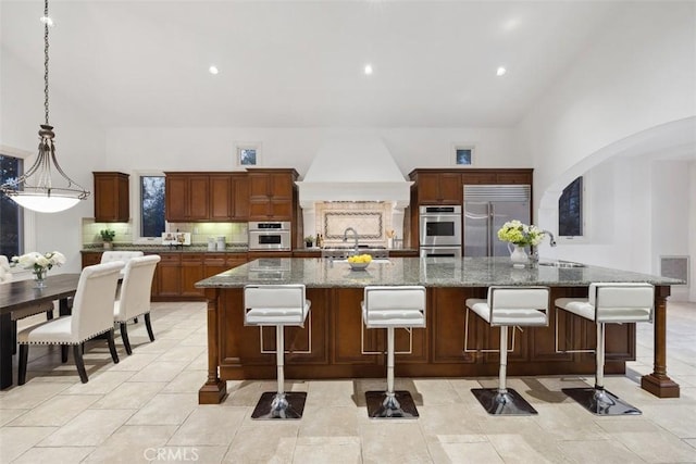 kitchen with arched walkways, decorative backsplash, appliances with stainless steel finishes, a sink, and premium range hood