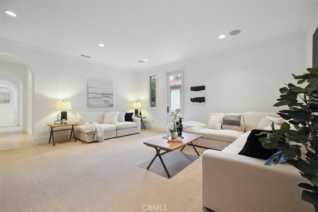 carpeted living area featuring arched walkways, crown molding, baseboards, and recessed lighting