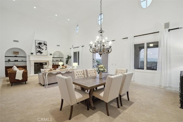 dining room with a chandelier, a high ceiling, visible vents, built in features, and a glass covered fireplace