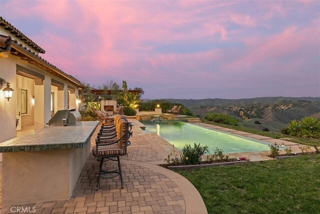 outdoor pool featuring a patio area, a grill, a mountain view, and an outdoor kitchen