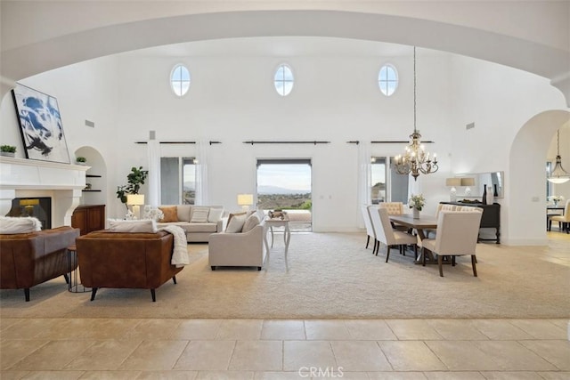 living area featuring light carpet, a high ceiling, a notable chandelier, and a glass covered fireplace