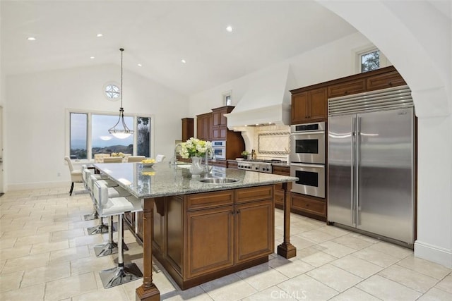 kitchen with a breakfast bar, custom range hood, appliances with stainless steel finishes, a sink, and high vaulted ceiling