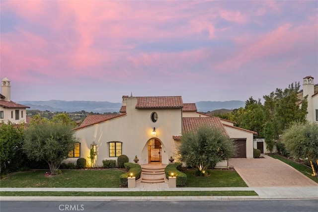 mediterranean / spanish-style home with decorative driveway, a tile roof, a yard, stucco siding, and a garage