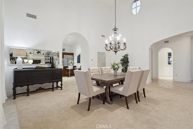 dining room featuring arched walkways, a high ceiling, visible vents, and light colored carpet