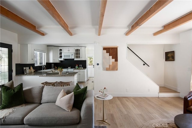 living area with light wood-style floors, beamed ceiling, baseboards, and stairs