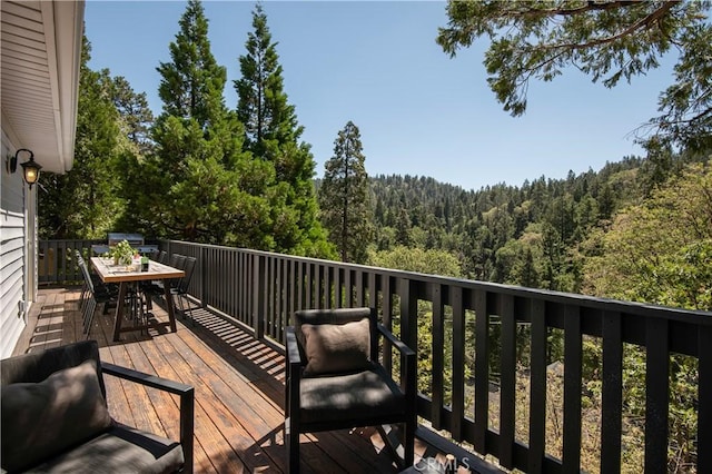 wooden terrace featuring a forest view and outdoor dining area