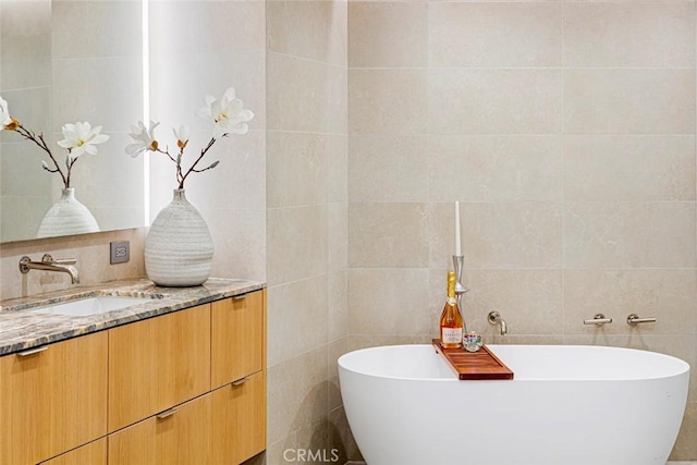 full bath featuring tile walls, vanity, and a freestanding bath