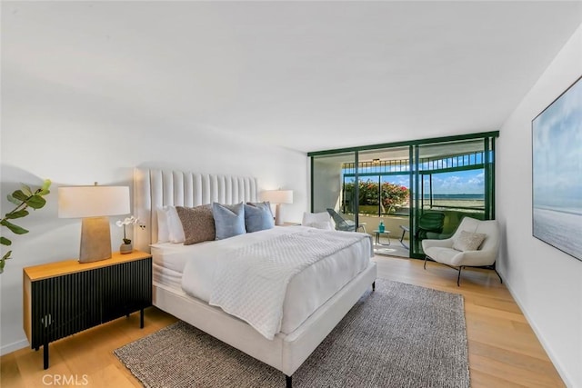 bedroom featuring light wood-style flooring, baseboards, access to outside, and a wall of windows