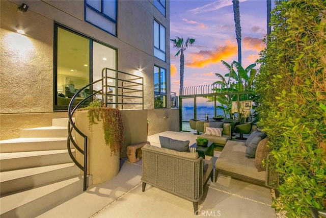 patio terrace at dusk featuring a balcony, a water view, and an outdoor living space