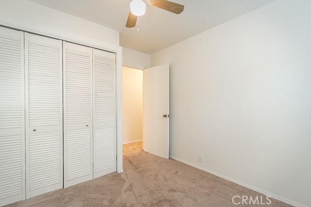 unfurnished bedroom featuring a closet, light colored carpet, ceiling fan, and baseboards