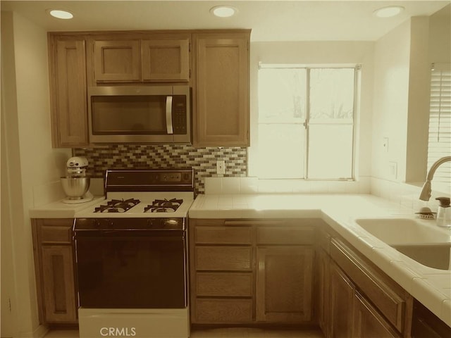 kitchen with stainless steel microwave, a sink, backsplash, and white gas range