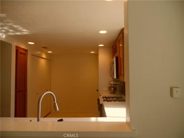 kitchen featuring brown cabinets, gas range gas stove, recessed lighting, stainless steel microwave, and a sink