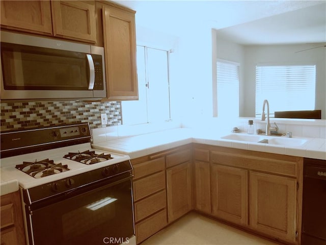 kitchen featuring tile counters, tasteful backsplash, stainless steel microwave, gas stove, and a sink