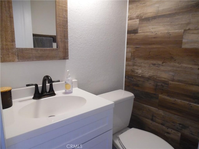 bathroom with toilet, vanity, and a textured wall