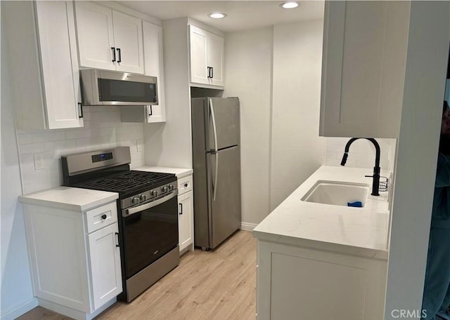 kitchen with stainless steel appliances, a sink, white cabinetry, and light wood-style floors