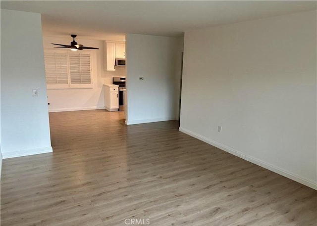 spare room with light wood finished floors, a ceiling fan, and baseboards