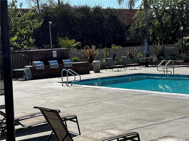 community pool with a patio area, fence, and a grill