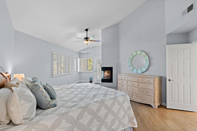 bedroom featuring visible vents, a glass covered fireplace, ceiling fan, vaulted ceiling, and wood finished floors