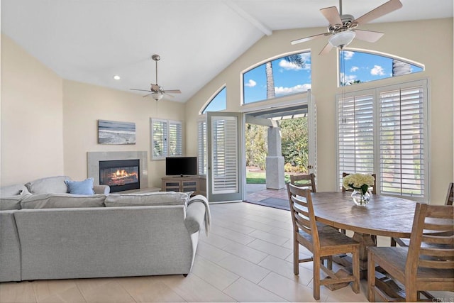 living room featuring light tile patterned floors, beamed ceiling, a glass covered fireplace, and a ceiling fan