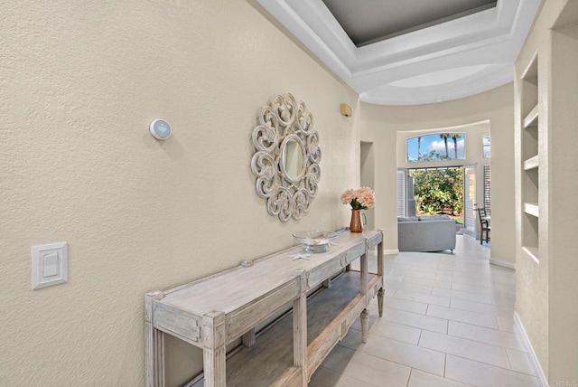 corridor featuring light tile patterned floors, a textured wall, a towering ceiling, baseboards, and a tray ceiling