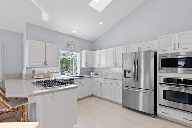 kitchen with a skylight, appliances with stainless steel finishes, a peninsula, white cabinetry, and a sink