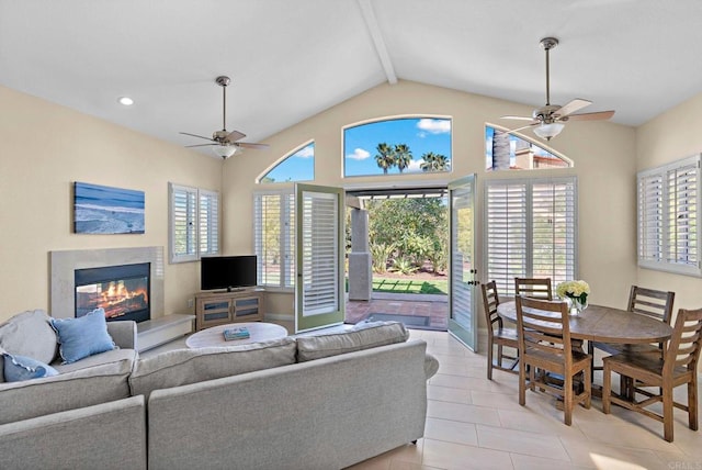 living area with a wealth of natural light, a glass covered fireplace, ceiling fan, and lofted ceiling with beams