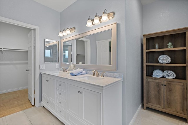 bathroom featuring double vanity, a sink, a walk in closet, and tile patterned floors