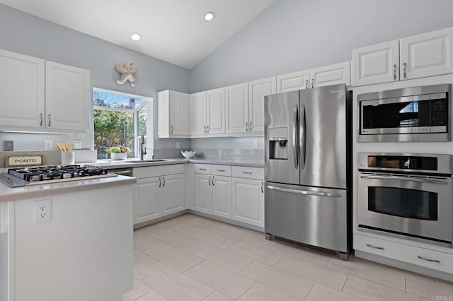 kitchen with white cabinets, lofted ceiling, appliances with stainless steel finishes, a peninsula, and a sink