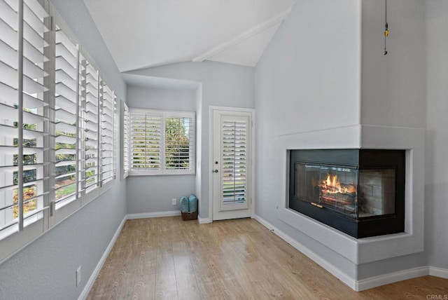 interior space with vaulted ceiling, wood finished floors, a multi sided fireplace, and baseboards