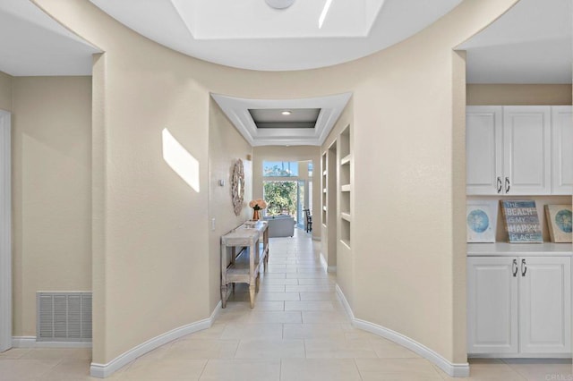 corridor featuring light tile patterned floors, visible vents, baseboards, built in features, and a raised ceiling