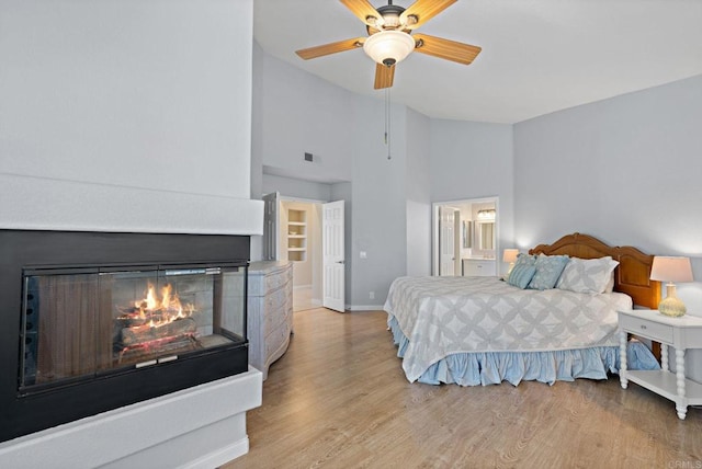 bedroom with a glass covered fireplace, visible vents, baseboards, light wood-type flooring, and ensuite bath