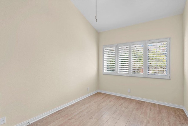 spare room with vaulted ceiling, light wood-style flooring, and baseboards