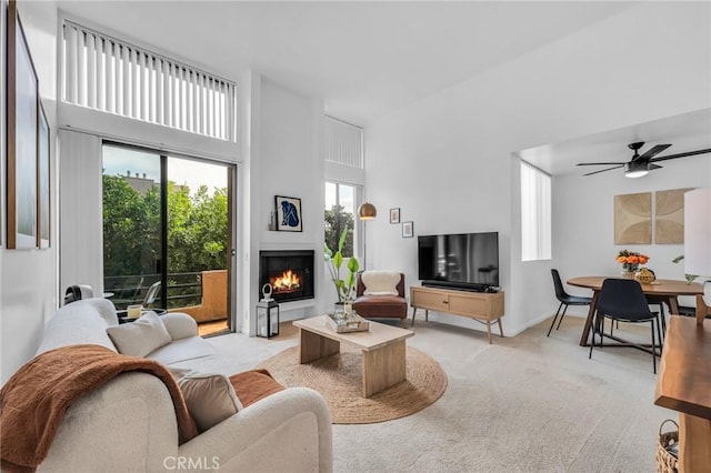 living area featuring ceiling fan, a lit fireplace, a wealth of natural light, and light colored carpet