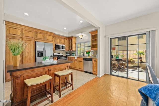 kitchen with a breakfast bar area, a sink, appliances with stainless steel finishes, backsplash, and glass insert cabinets