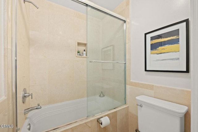 bathroom with toilet, bath / shower combo with glass door, and tile walls