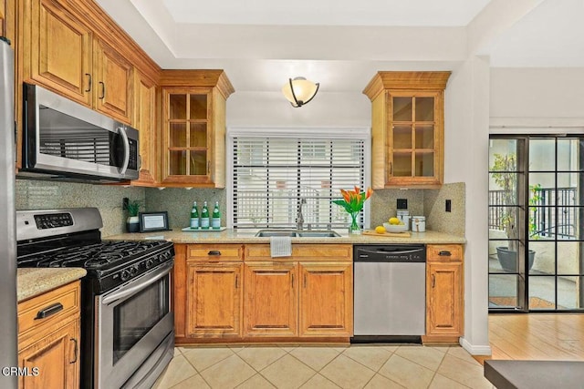 kitchen with light tile patterned floors, a sink, appliances with stainless steel finishes, decorative backsplash, and brown cabinetry