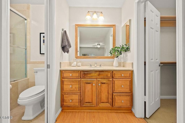 bathroom with a shower with shower door, vanity, toilet, and wood finished floors