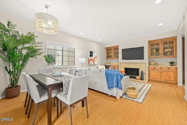 dining room featuring baseboards, a high end fireplace, light wood-style flooring, and recessed lighting