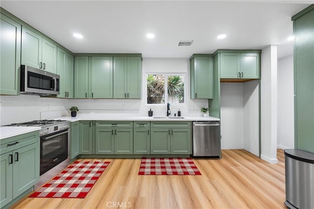 kitchen with stainless steel appliances, a sink, light countertops, and green cabinetry