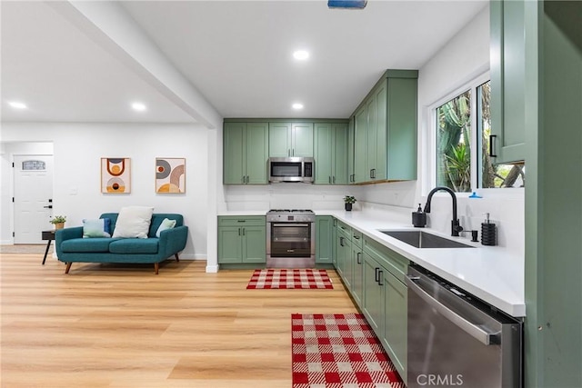 kitchen featuring green cabinetry, stainless steel appliances, light countertops, light wood-type flooring, and a sink