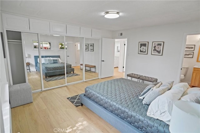 bedroom featuring a closet, visible vents, light wood-style flooring, and ensuite bathroom