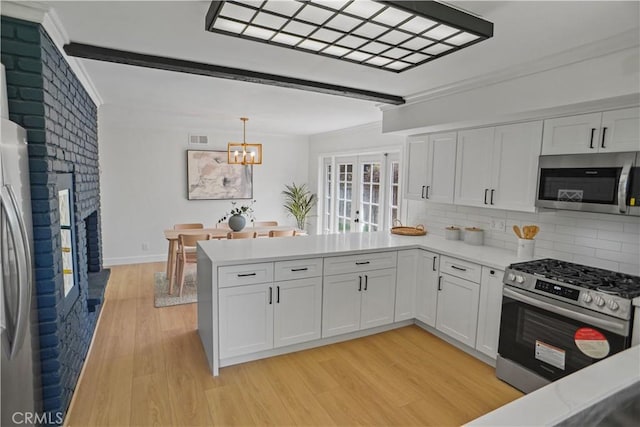 kitchen featuring appliances with stainless steel finishes, a brick fireplace, light countertops, and a peninsula