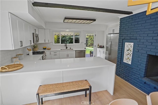 kitchen with a peninsula, stainless steel appliances, light countertops, white cabinetry, and a sink