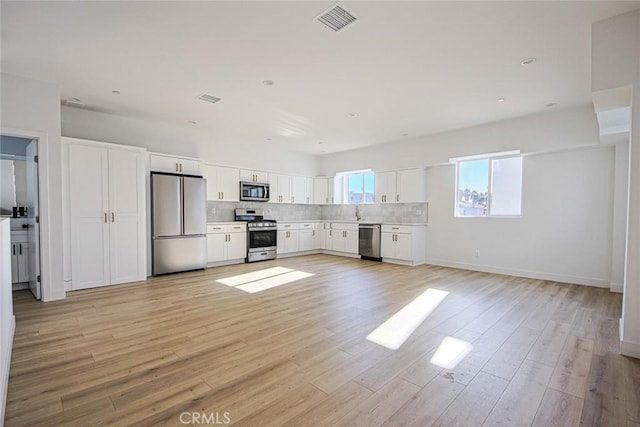 kitchen with tasteful backsplash, white cabinets, stainless steel appliances, light countertops, and light wood-type flooring