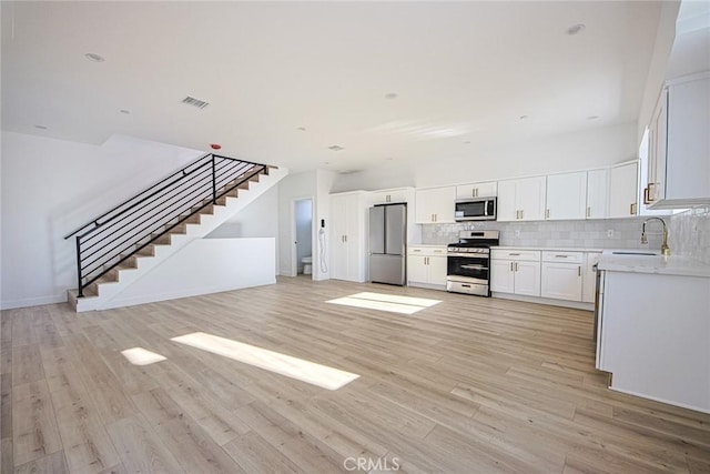 kitchen featuring light wood-style flooring, stainless steel appliances, a sink, visible vents, and backsplash