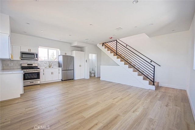 kitchen featuring light wood finished floors, light countertops, decorative backsplash, appliances with stainless steel finishes, and white cabinetry