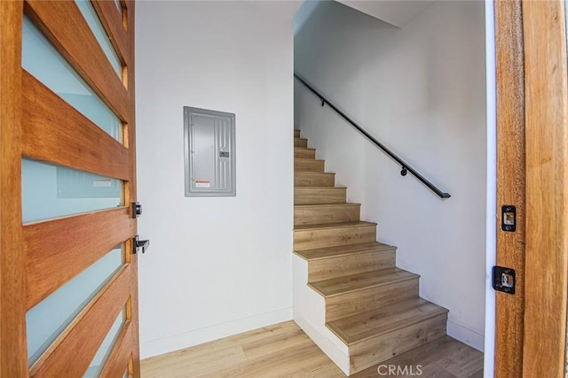 stairs featuring electric panel, baseboards, and wood finished floors