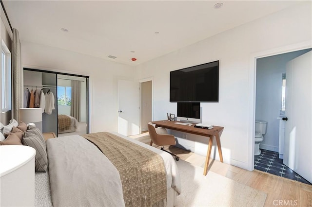 bedroom with a closet, visible vents, connected bathroom, wood finished floors, and baseboards